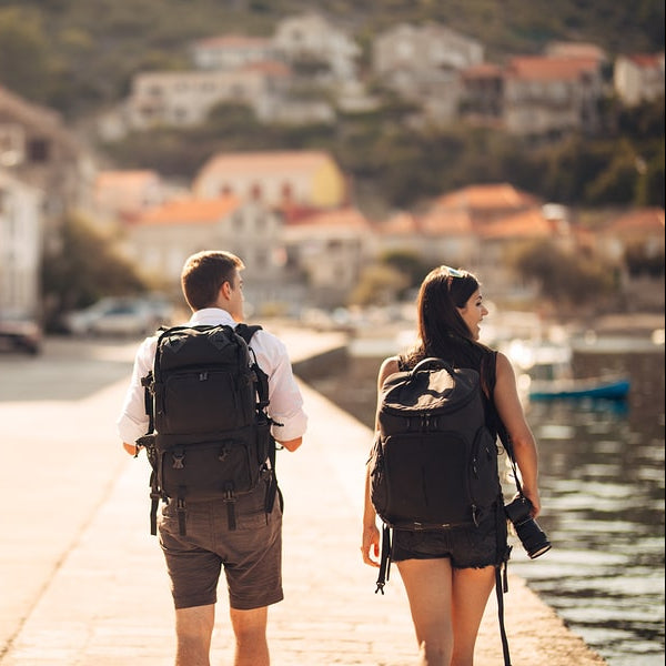 Two people with backpacks walking along a coastal street.